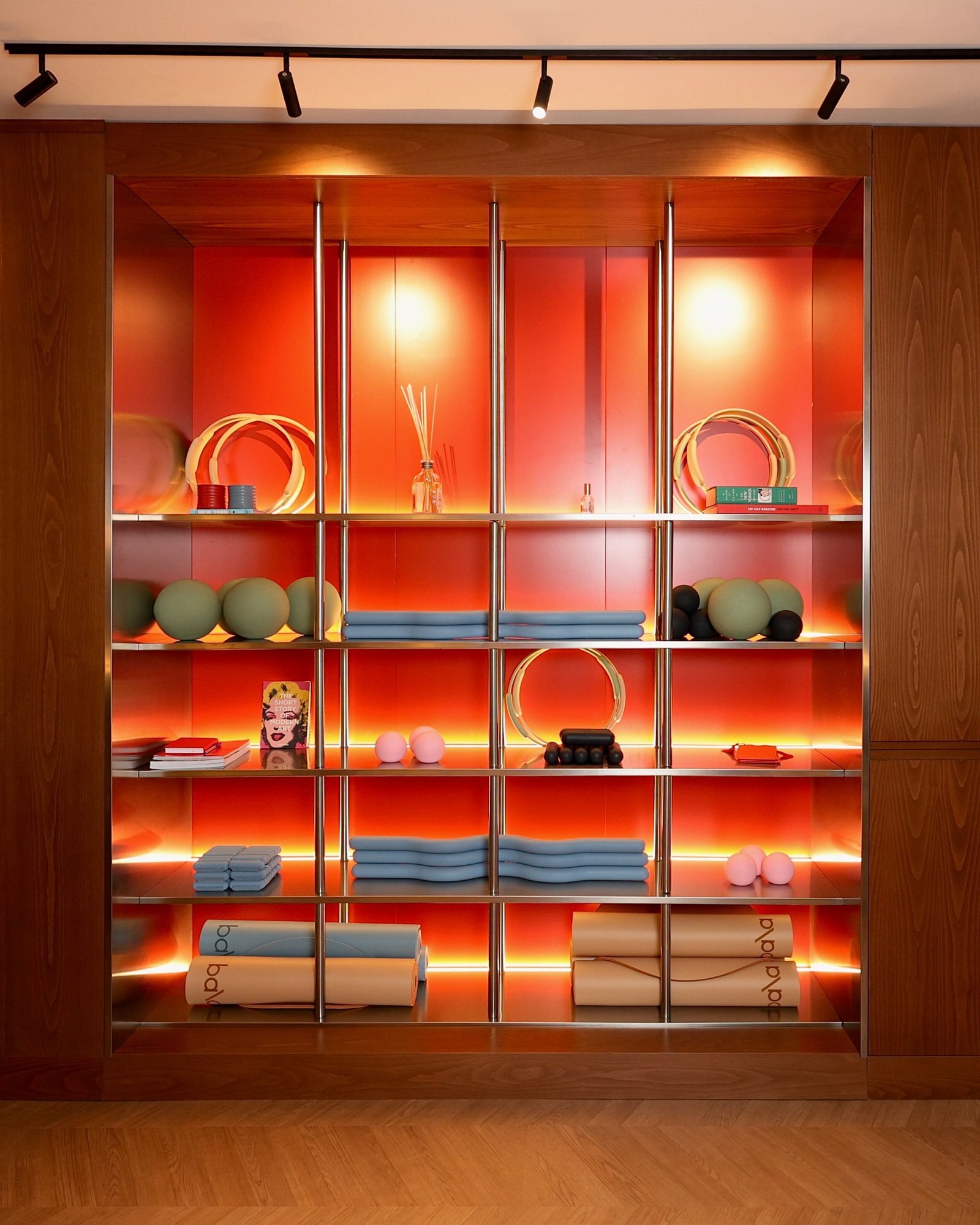 Full-height stainless steel equipment wall set into an oak frame and lit from behind each shelf at La Suite pilates studio